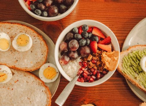 A fresh and vibrant breakfast flat lay featuring a yogurt bowl with fruits and toast with eggs and avocado.