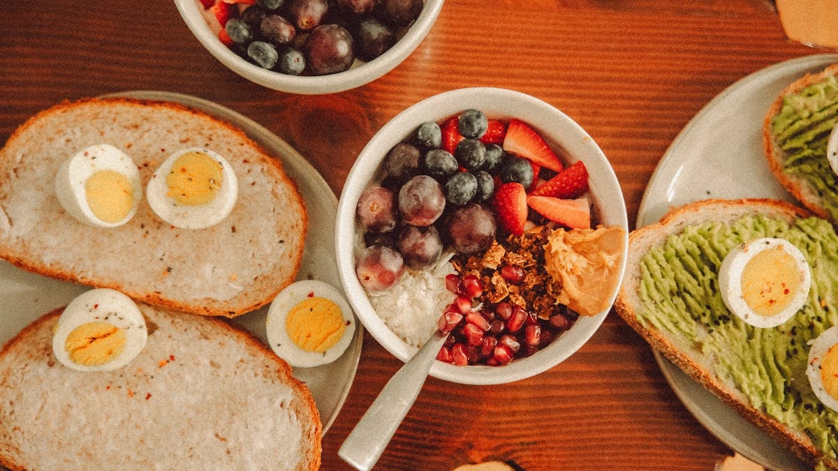 A fresh and vibrant breakfast flat lay featuring a yogurt bowl with fruits and toast with eggs and avocado.